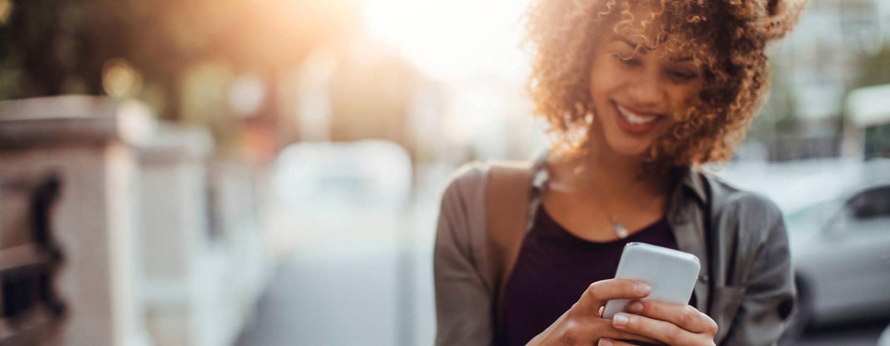 woman texts on her phone as she walks through the city