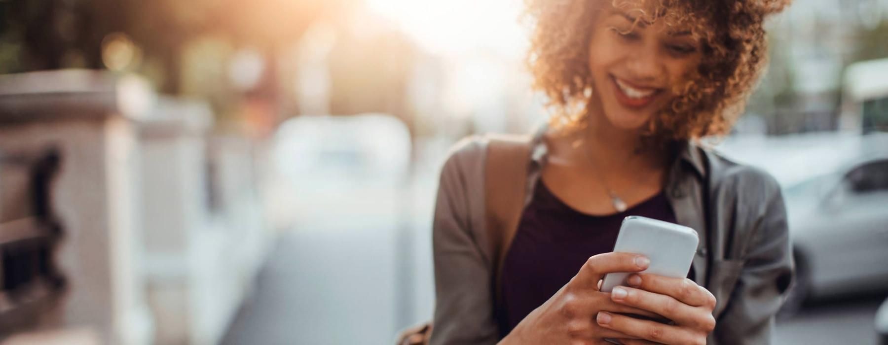 woman texts on her phone as she walks through the city